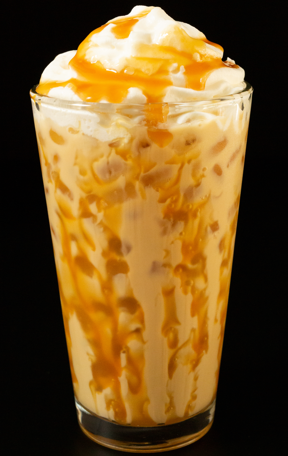 A pint glass has caramel dizzled all around the inside and is filled with a light brown butterbeer latte topped with whipped cream and caramel.
