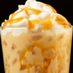 Close up of a butterbeer latte in a pint glass. Caramel has been drizzled all over the inside of the glass and on top of the whipped cream topping.