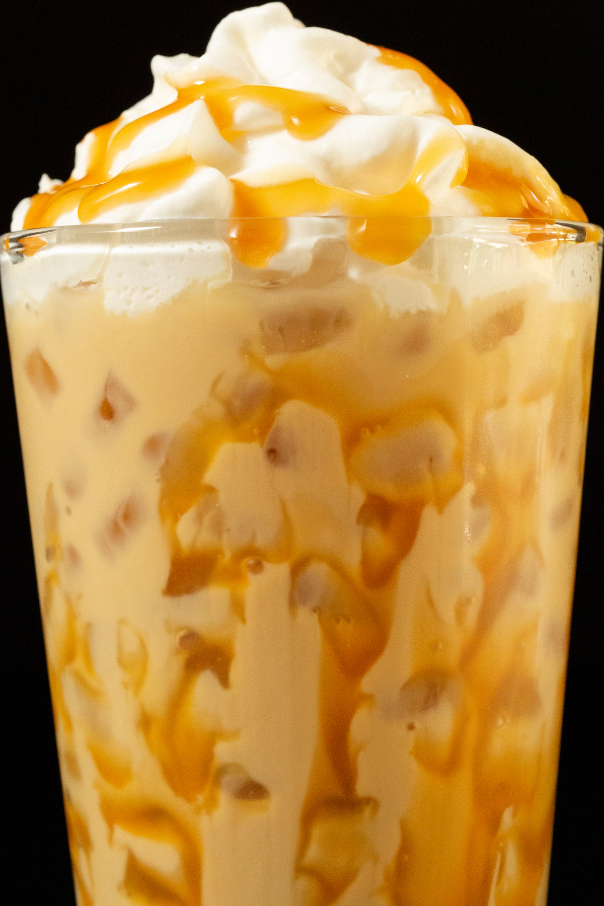 Close up of a butterbeer latte in a pint glass. Caramel has been drizzled all over the inside of the glass and on top of the whipped cream topping.