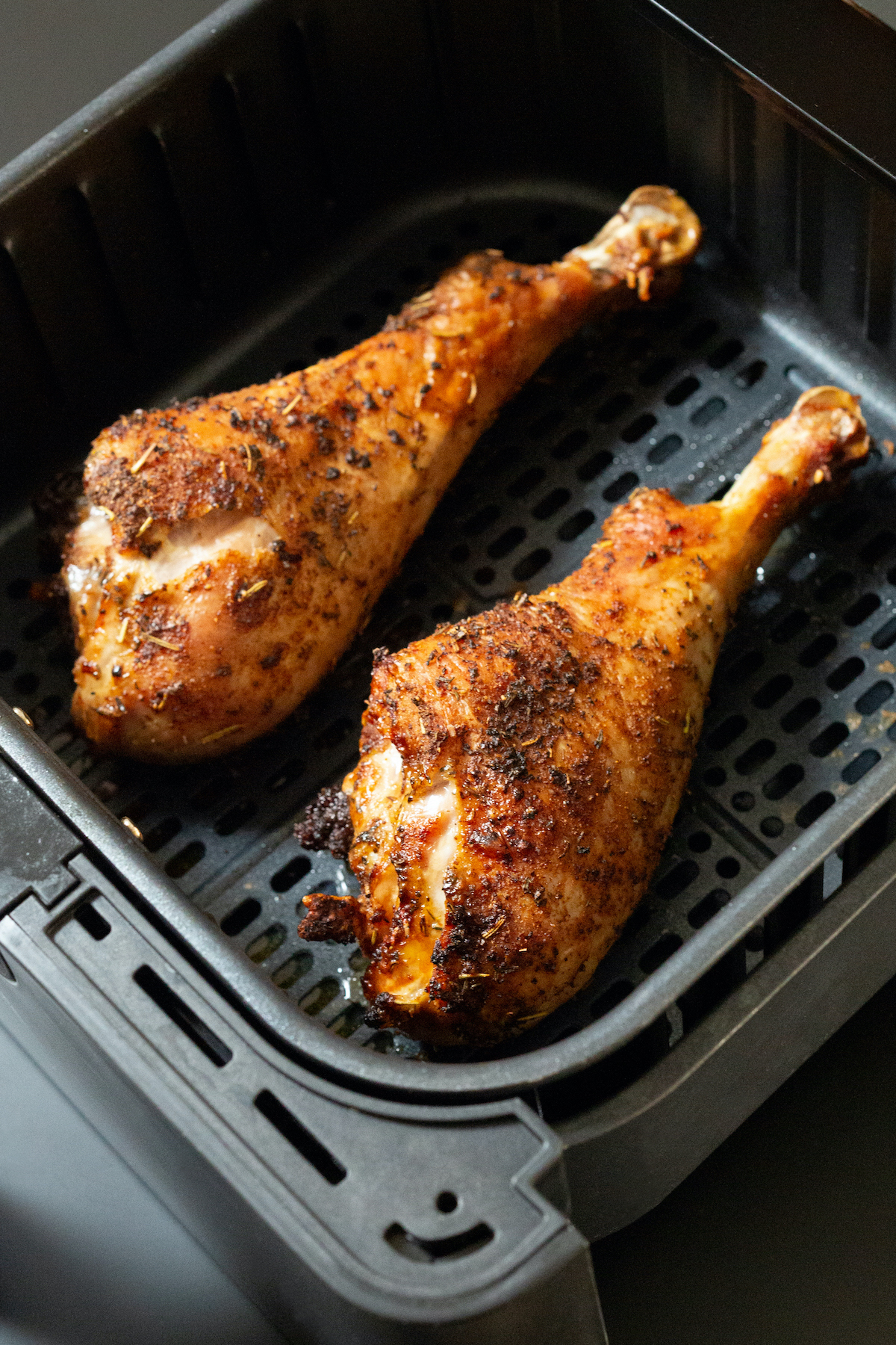 Golden brown cooked turkey legs in an air fryer basket.