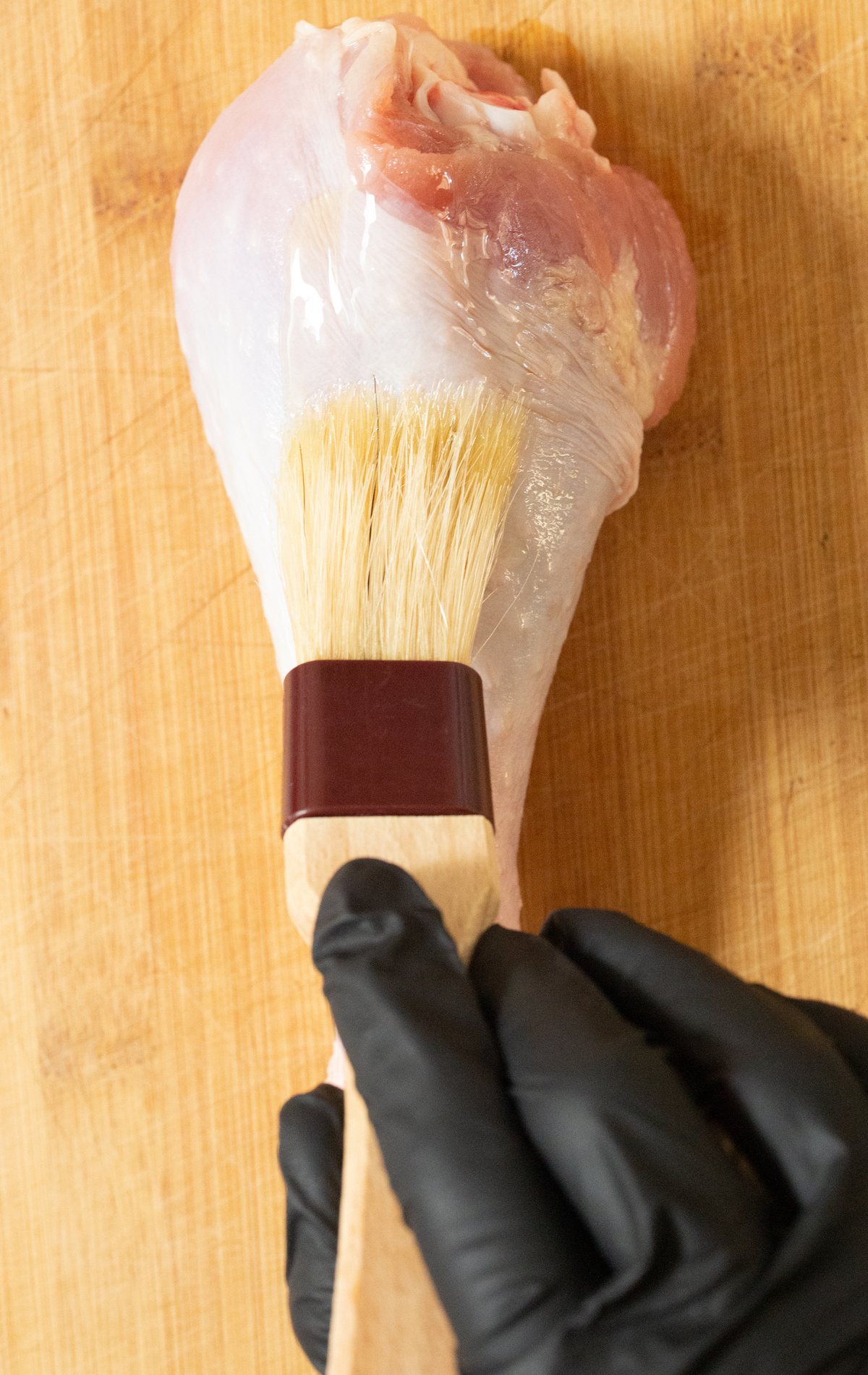 A raw turkey leg being brushed with oil via a pastry brush.