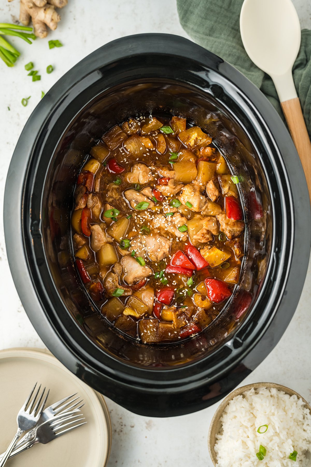 A crock pot that's filled with cooked sweet Hawaiian chicken with coarsely chopped red bell pepper and pineapple chunks.