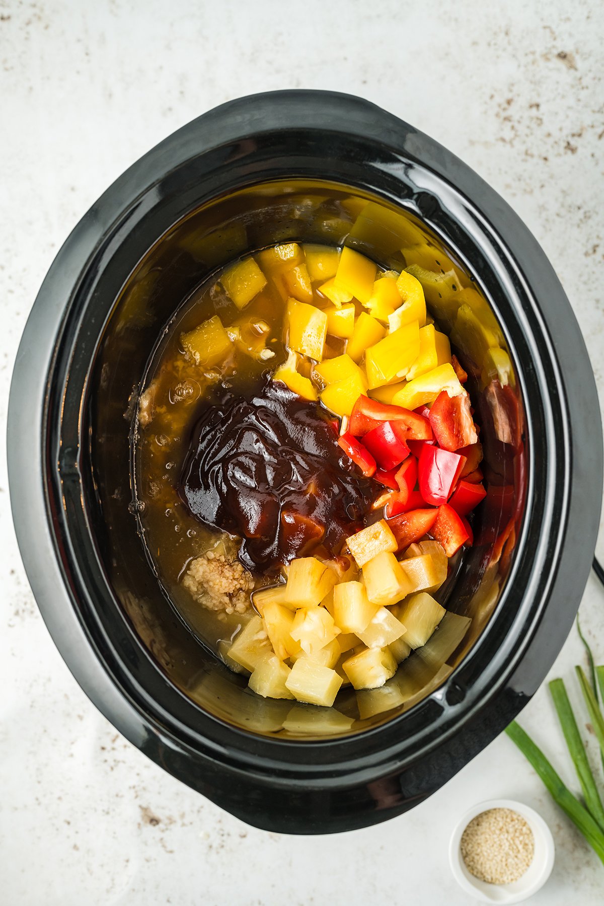 A crock pot filled with the ingredients to make sweet Hawaiian chicken before cooking.
