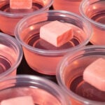 10 pink jello shots topped with unwrapped Starburst candies on a black background.