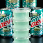 A stack of light blue baja blast jello shots in front of several cans of the soda.