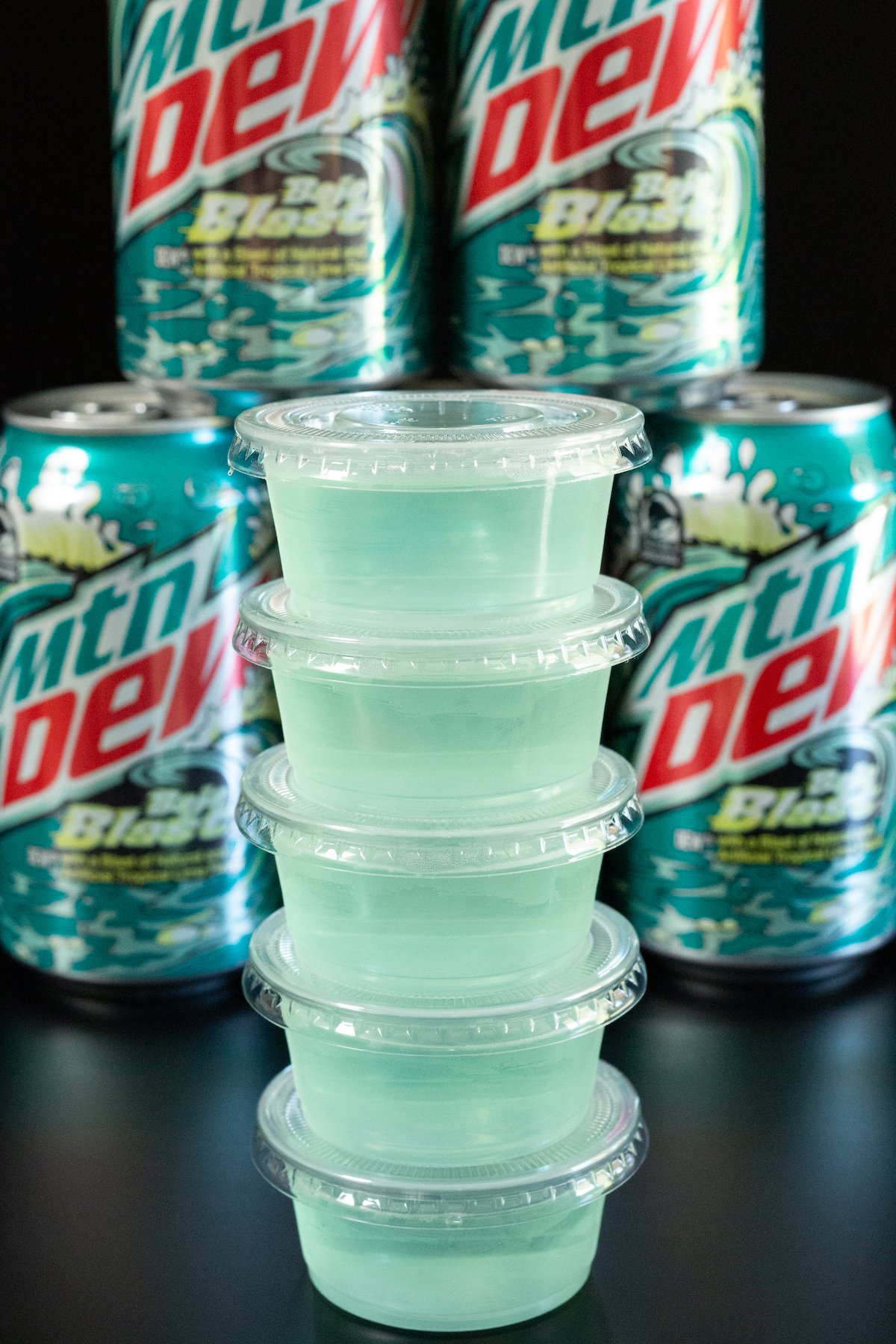 A stack of light blue baja blast jello shots in front of several cans of the soda.