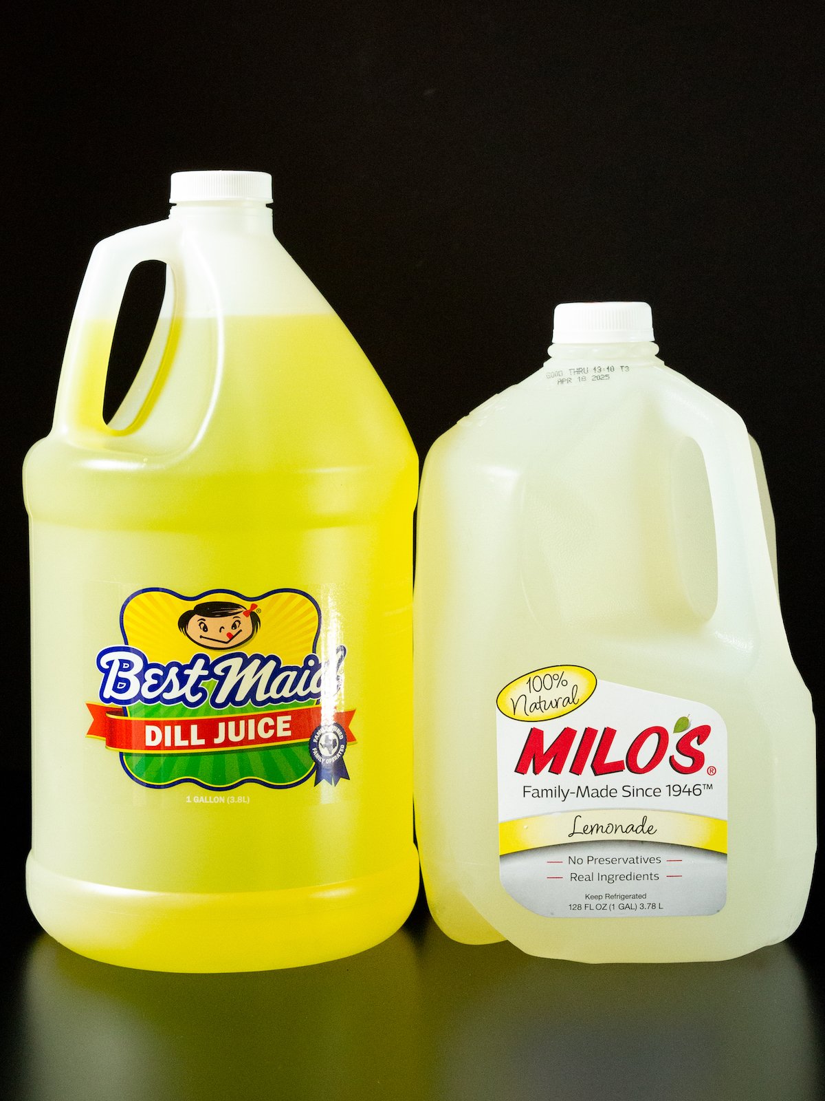 A gallon of dill pickle juice and a gallon jug of Milo's lemonade on a black background.