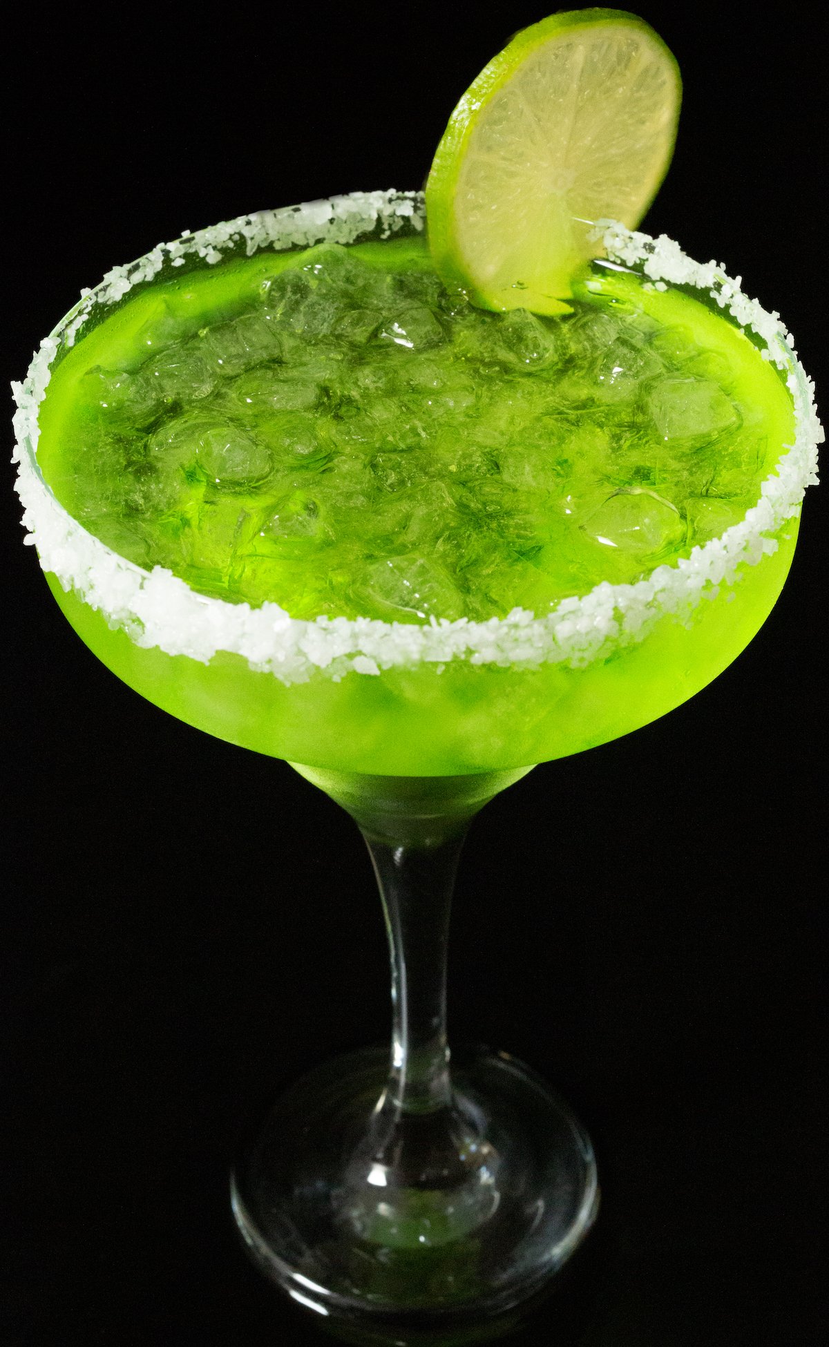 A classic tall margarita glass is rimmed with coarse salt, filled with a neon green cocktail, and garnished with a lime wheel.