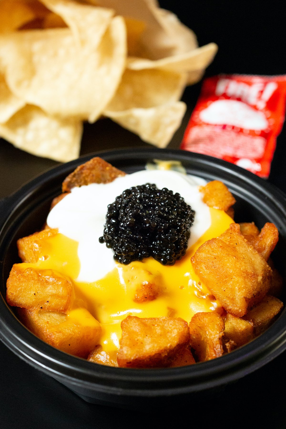 A bowl of Taco Bell cheesy fiesta potatoes with a generous scoop of caviar. Tortilla chips are out of focus in the background.
