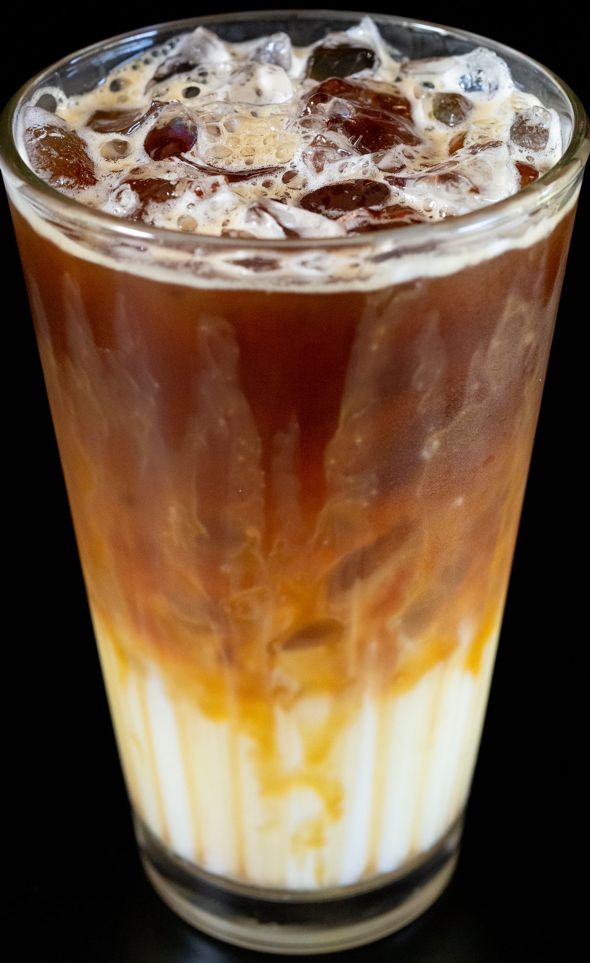 A pint glass has caramel dripping down the insides and is filled 1/3 with milk, and the top 2/3 with espresso.