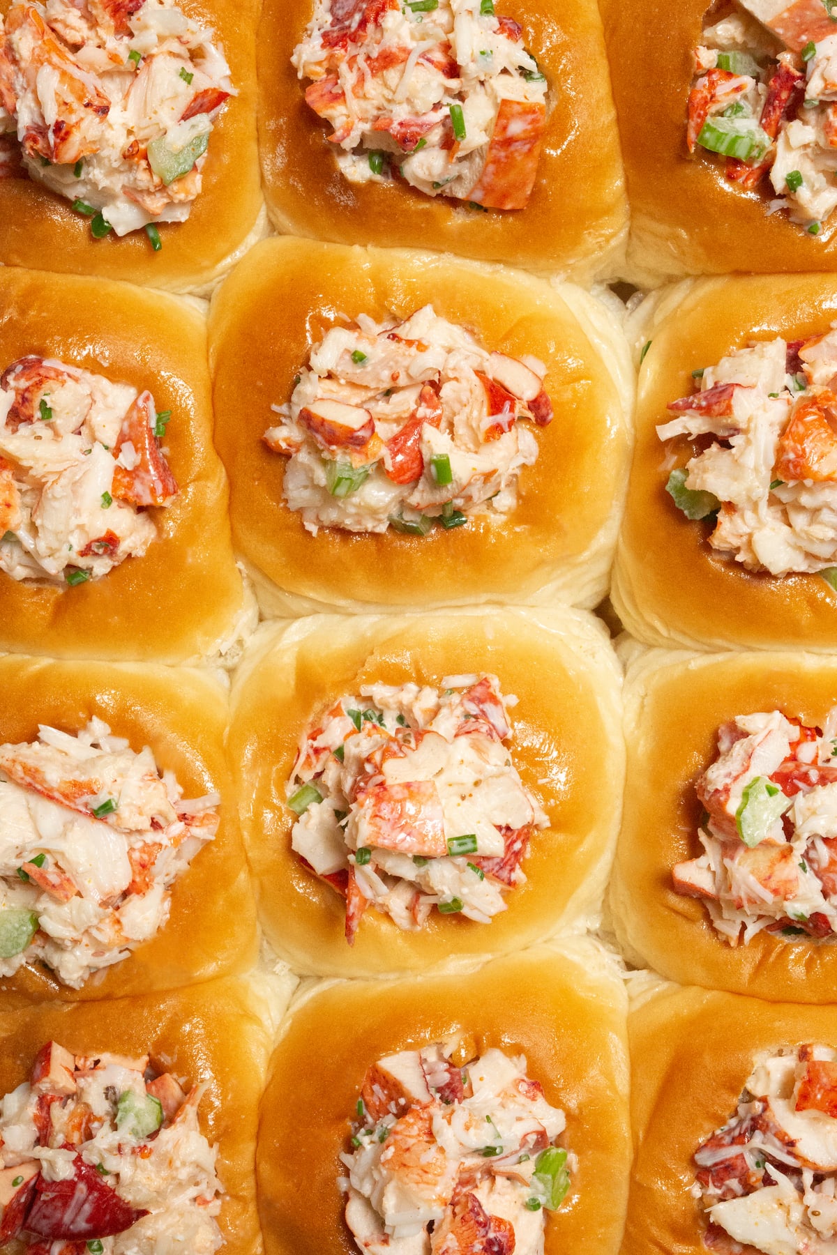 Overhead view of a pack of 12 Hawaiian rolls that have had holes cut in the middle and stuffed with cold lobster salad.