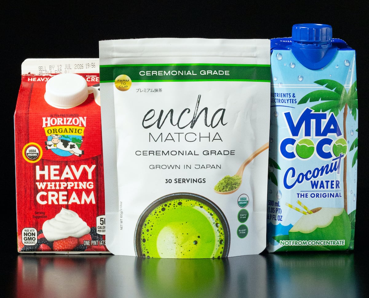 A pint of heavy creamy, bag of ceremonial grade matcha, and a bottle of coconut water on a black background.