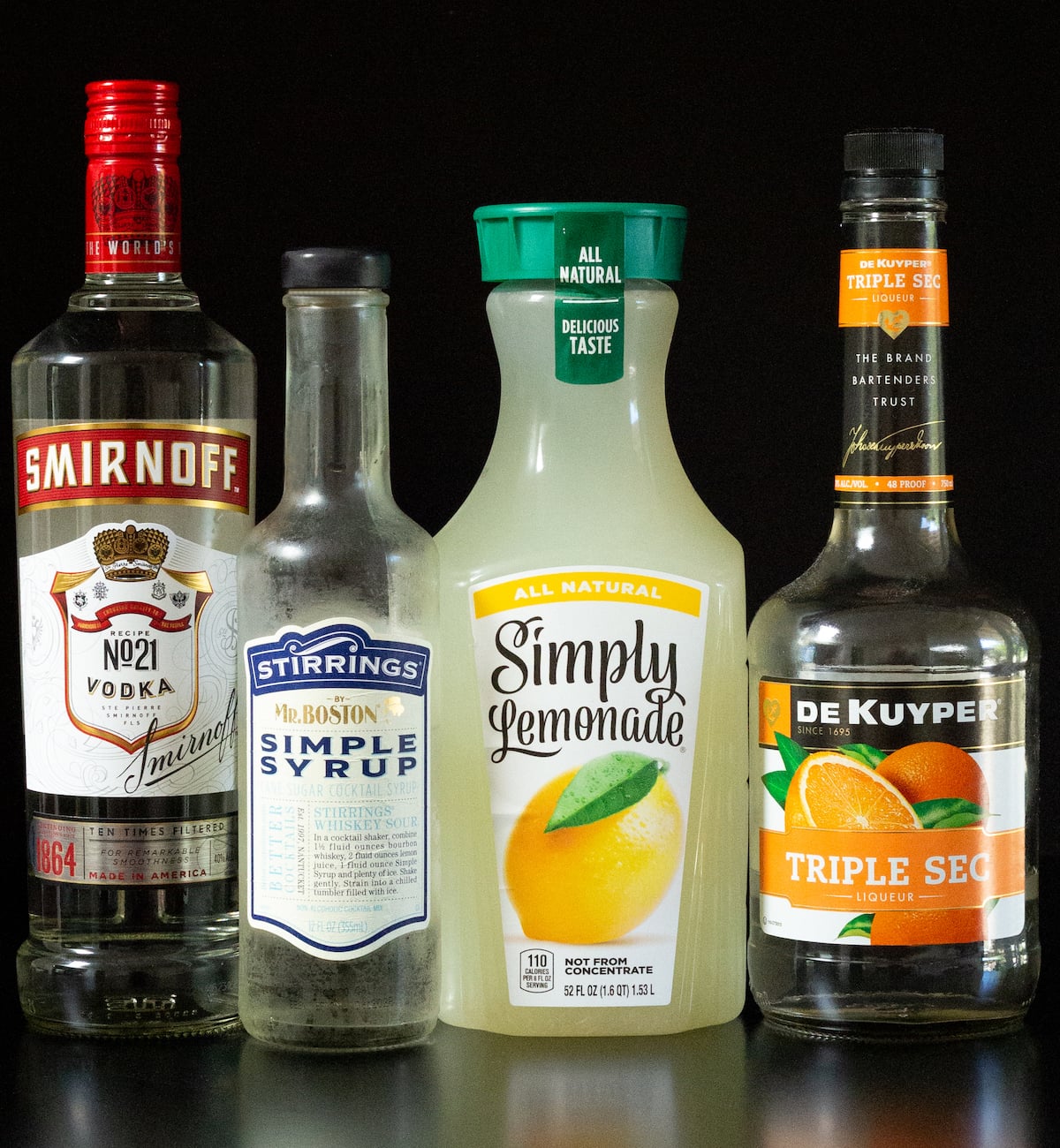 A bottle of Smirnoff vodka, simple syrup, Simply lemonade, and triple sec all on a black background.