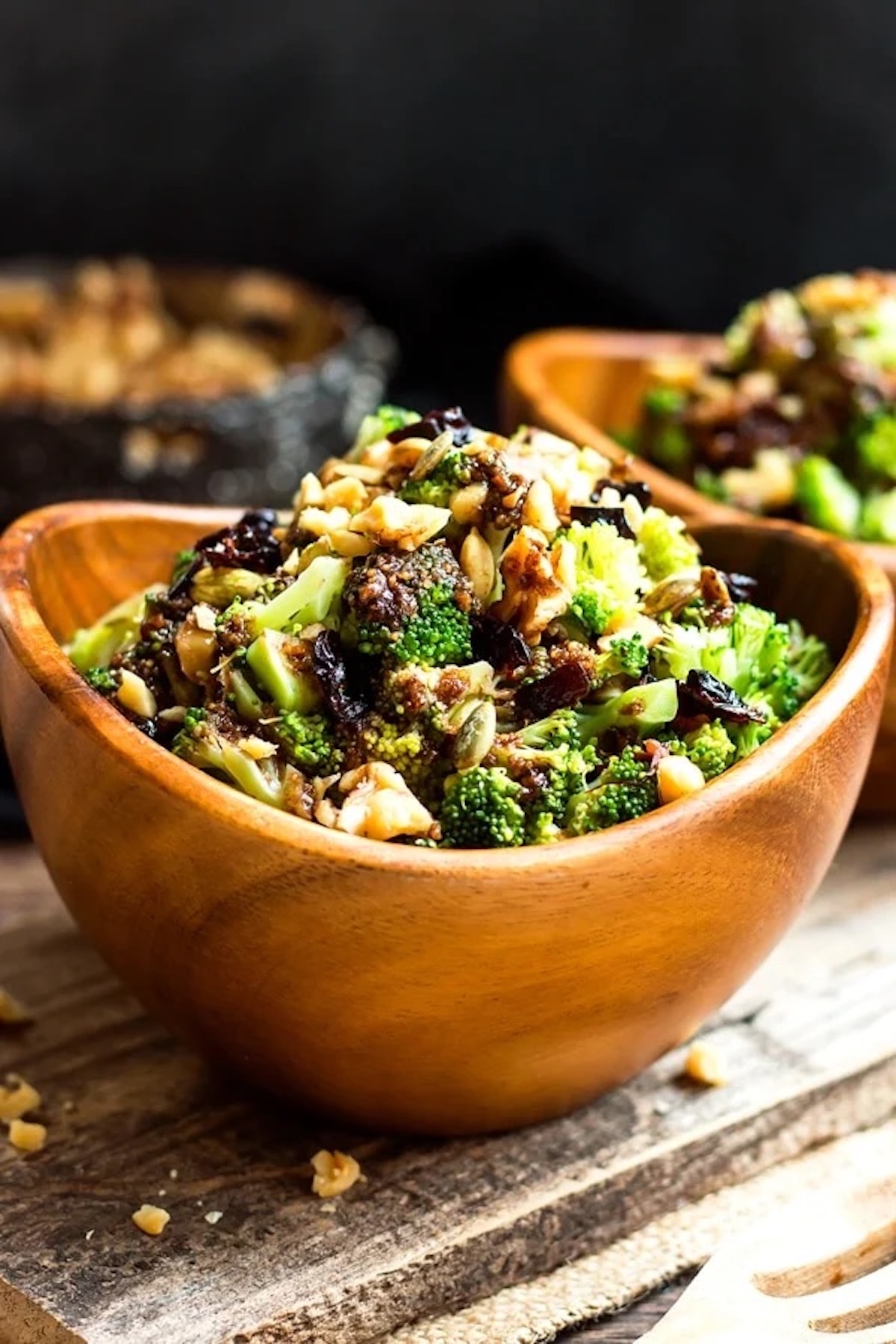 An oval wooden bowl filled with a chopped broccoli salad with dried cranberries and nuts.
