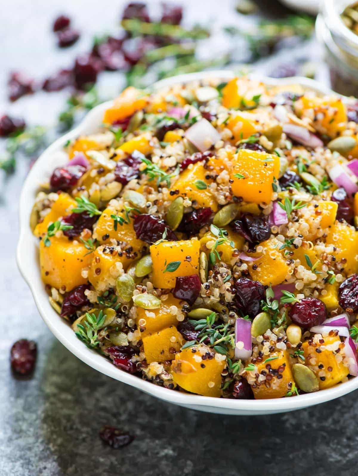 A white bowl filled with a quinoa salad that has large cubes of squash, diced red onion, peptides, and chopped herbs.