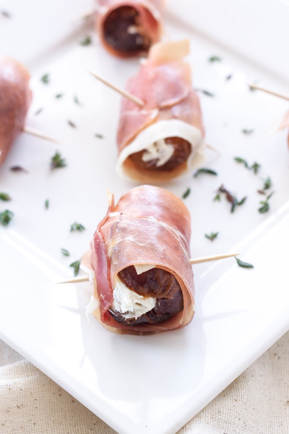 A white serving plate filled with prosciutto wrapped dates that are stuffed with goat cheese.