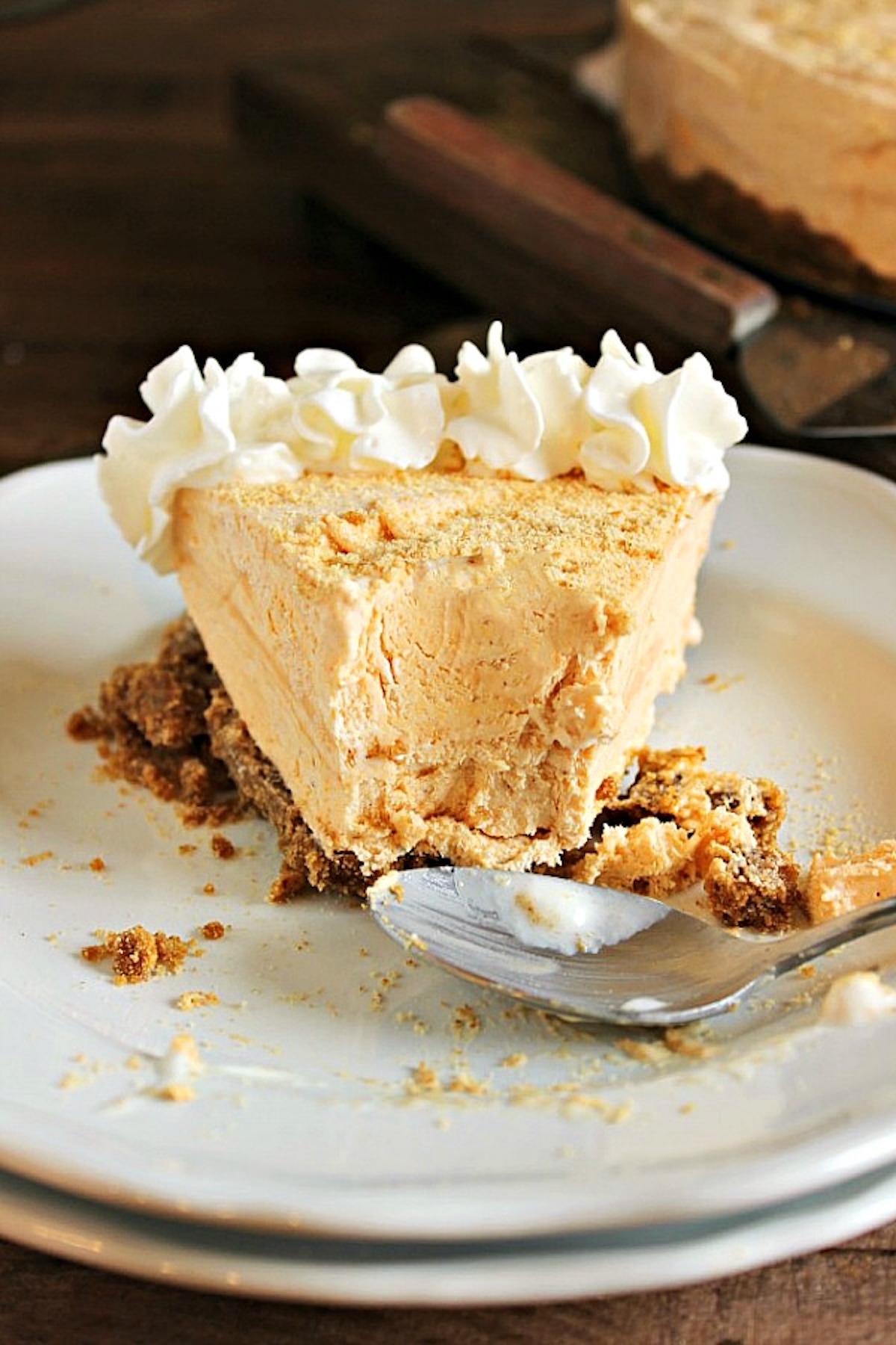 A frozen slice of pumpkin cheesecake on a white serving dish. About half the slice has been eaten, a dirty spoon sits in front.