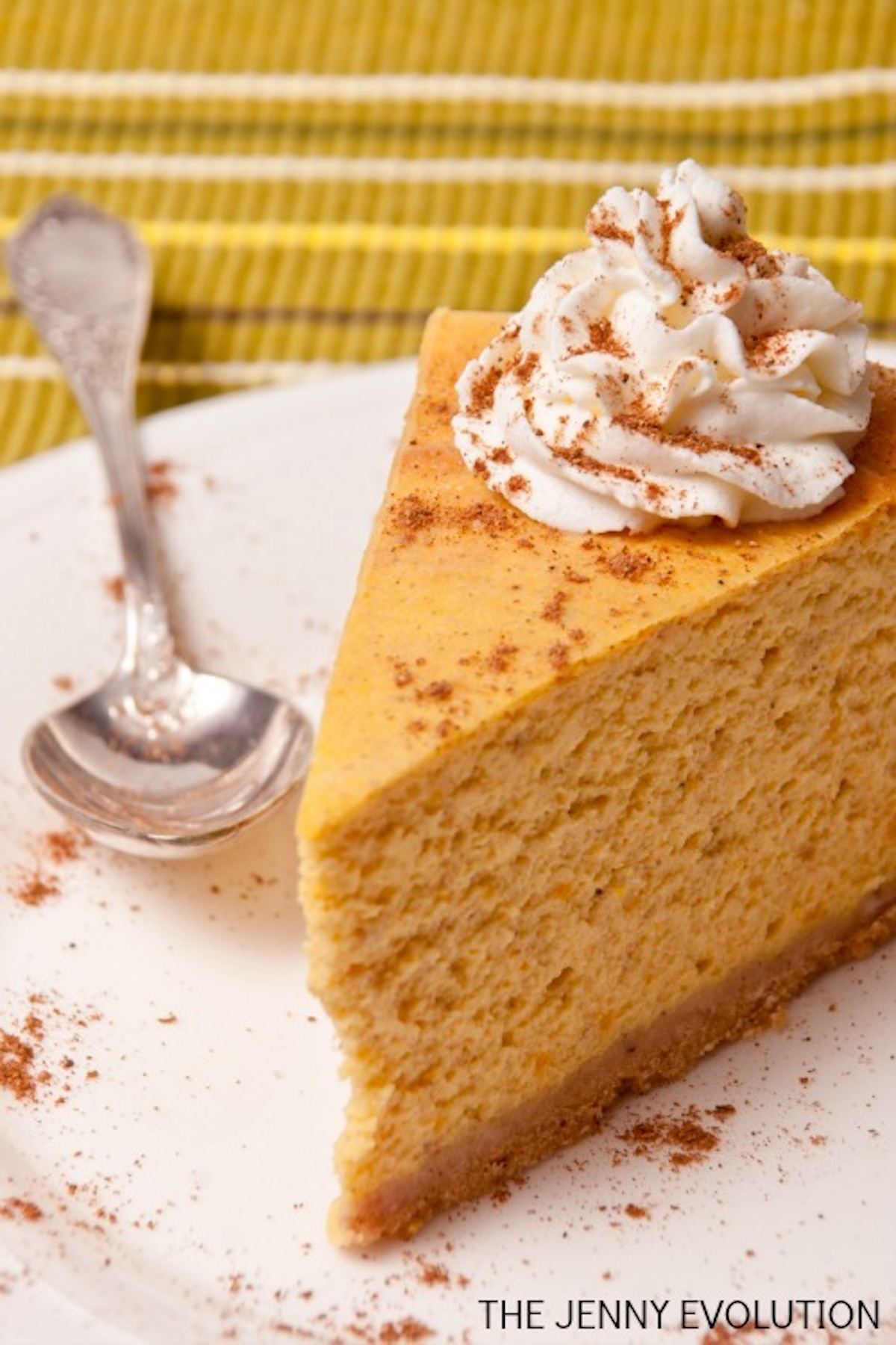 A thick slide of orange pumpkin cheesecake with a dollop of whipped cream.