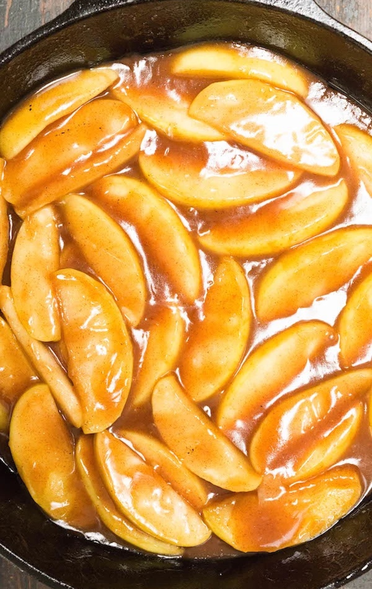 A cast iron skillet filled with sliced apples coated in a thick cinnamon sugar sauce.
