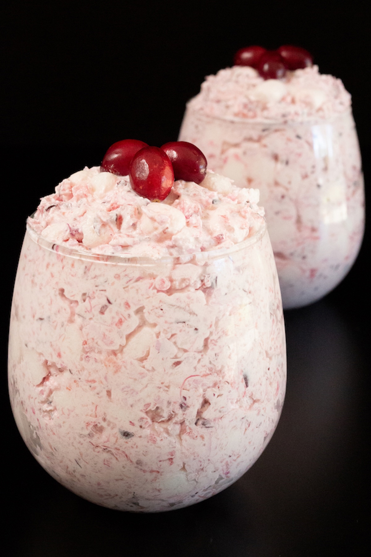 Two stemless wine glass filled to the top with a cranberry fluff that's topped with three fresh cranberries each.