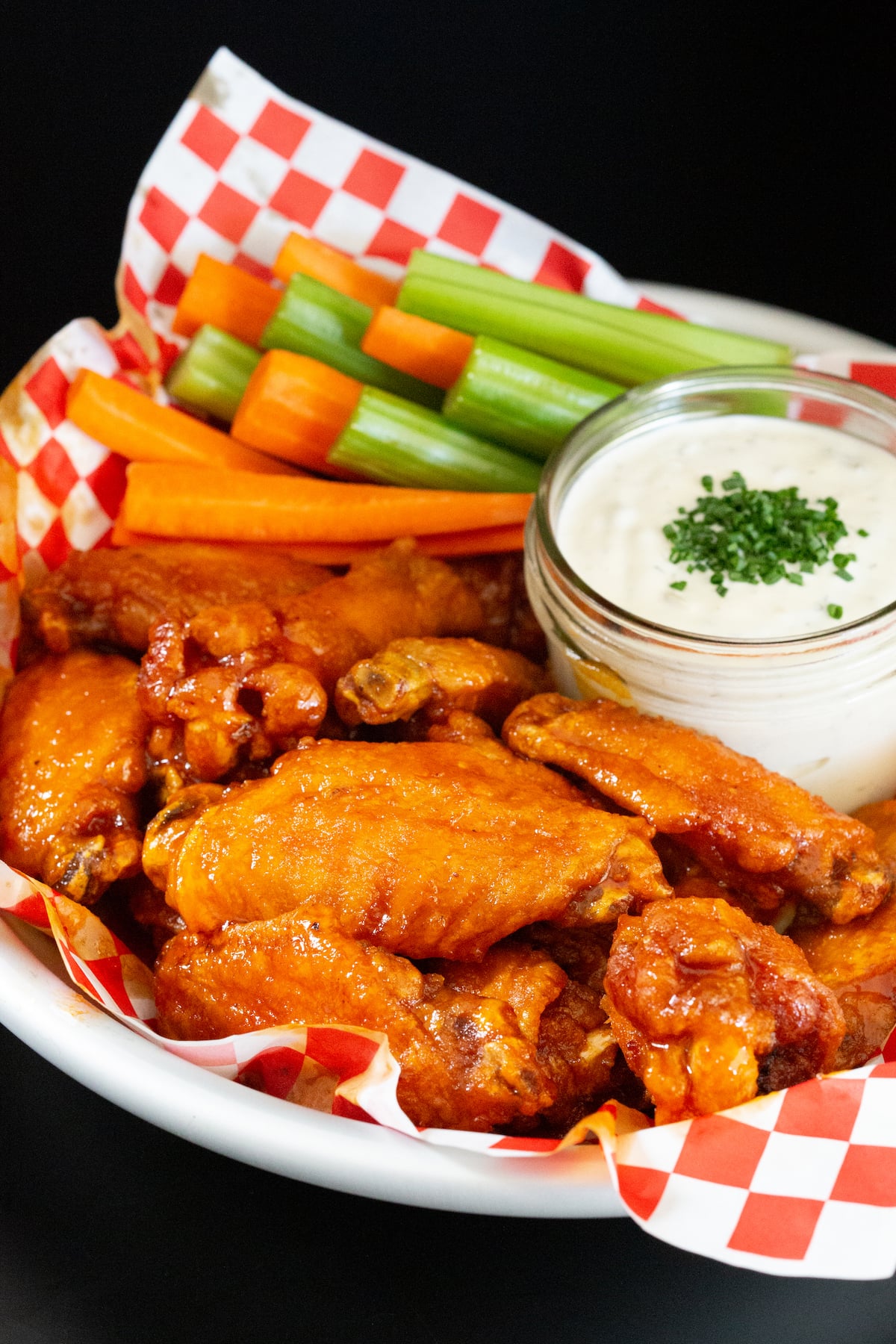 A basket of hot honey buffalo wings with a jar of ranch dressing and celery and carrot sticks.