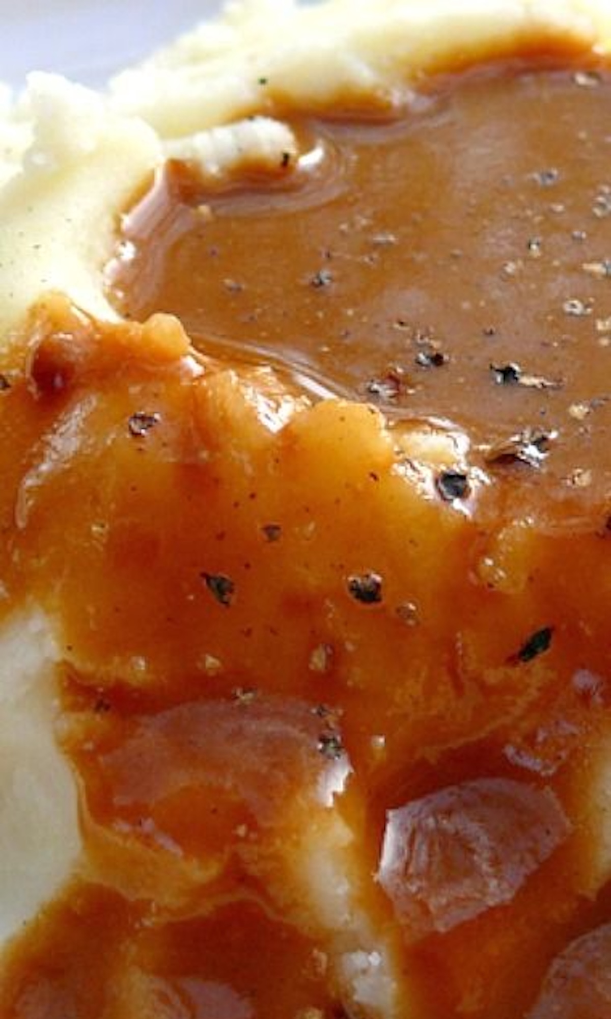 A pile of mashed potatoes generously overflowing with dark brown gravy that has large specs of black peppers.