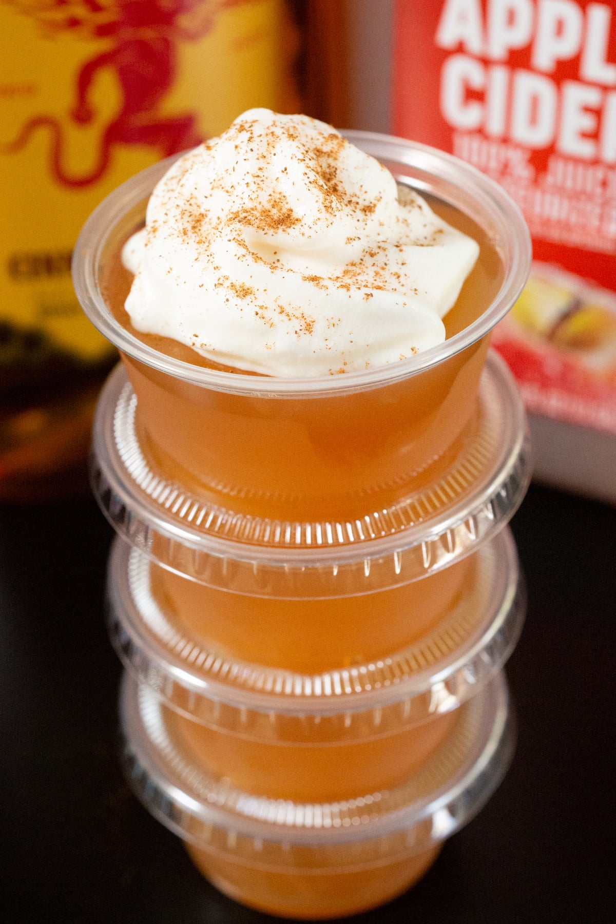A stack of apple cider jello shots in front of a bottle of Fireball and a gallon of apple cider.