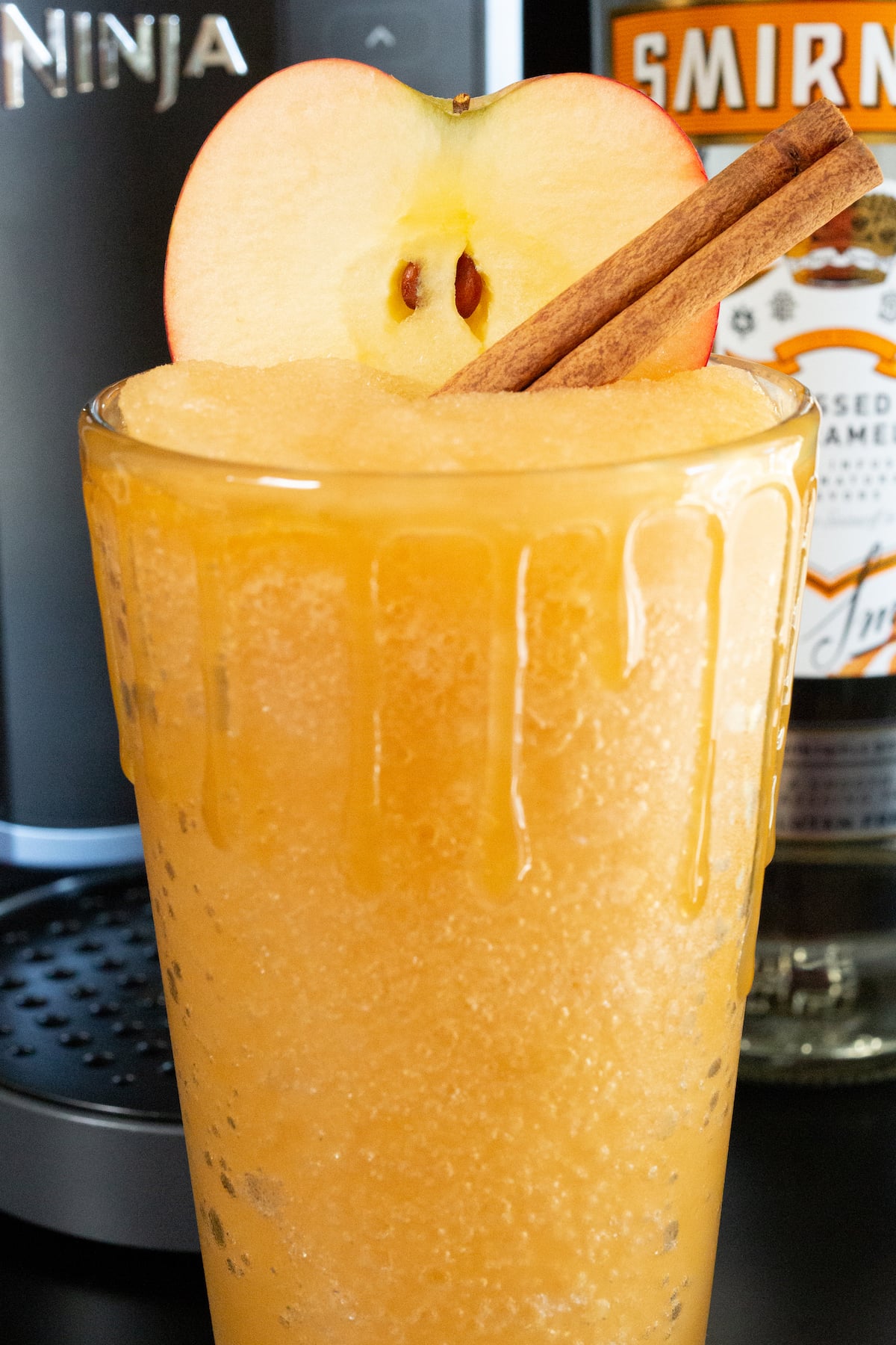 A pint glass filled with an apple cider slushy has caramel dripping down it's sides.