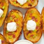 Several loaded potato skins on a white serving dish.