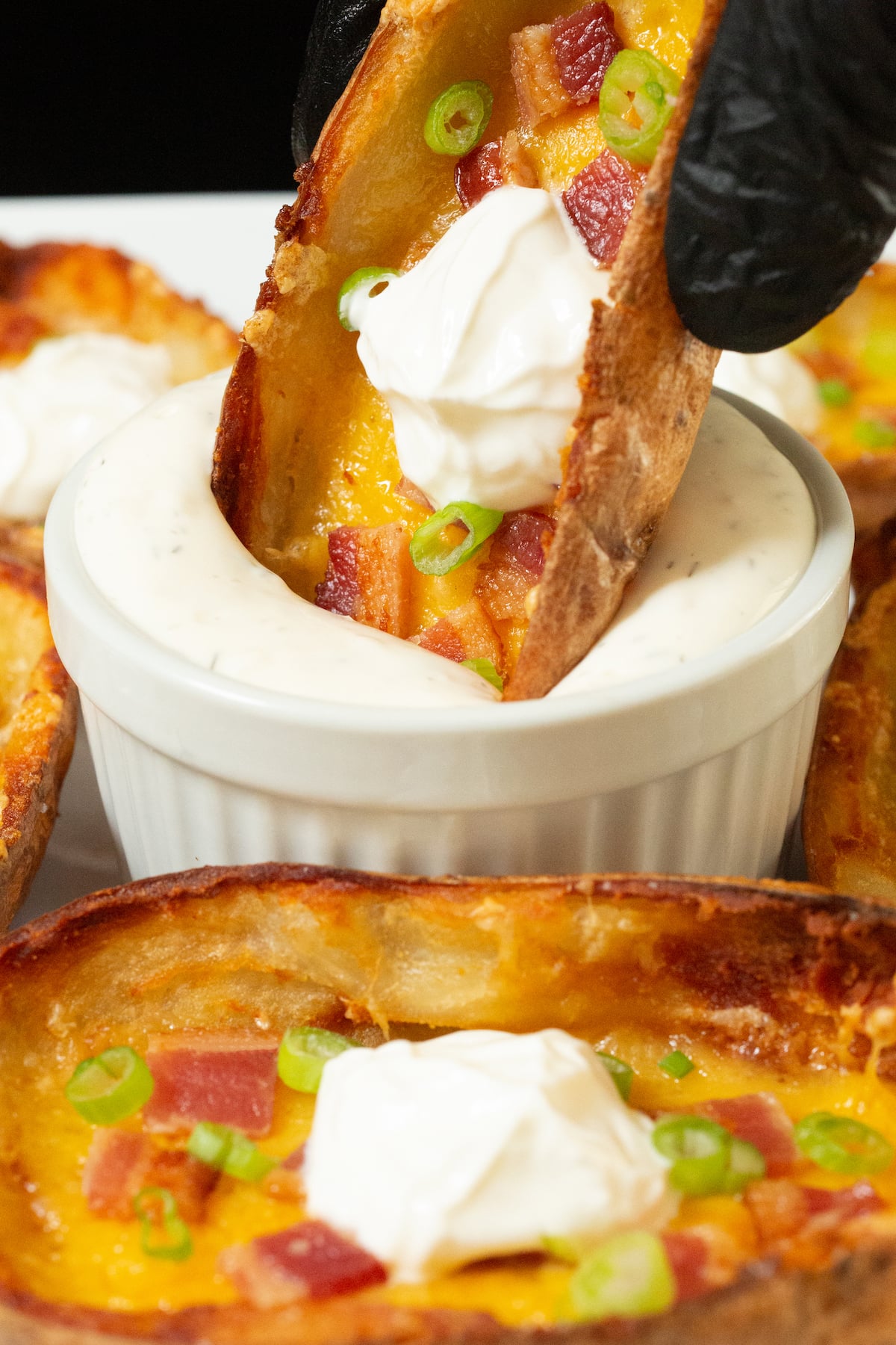 A gloved hand dips a potato skin into a ramekin of ranch dressing.